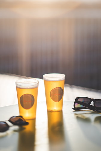 Two glasses of beer and sunglasses on a table in sunlight