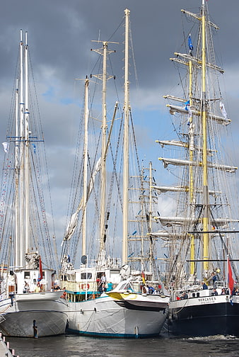 Tall sailing ships docked in harbor under cloudy sky