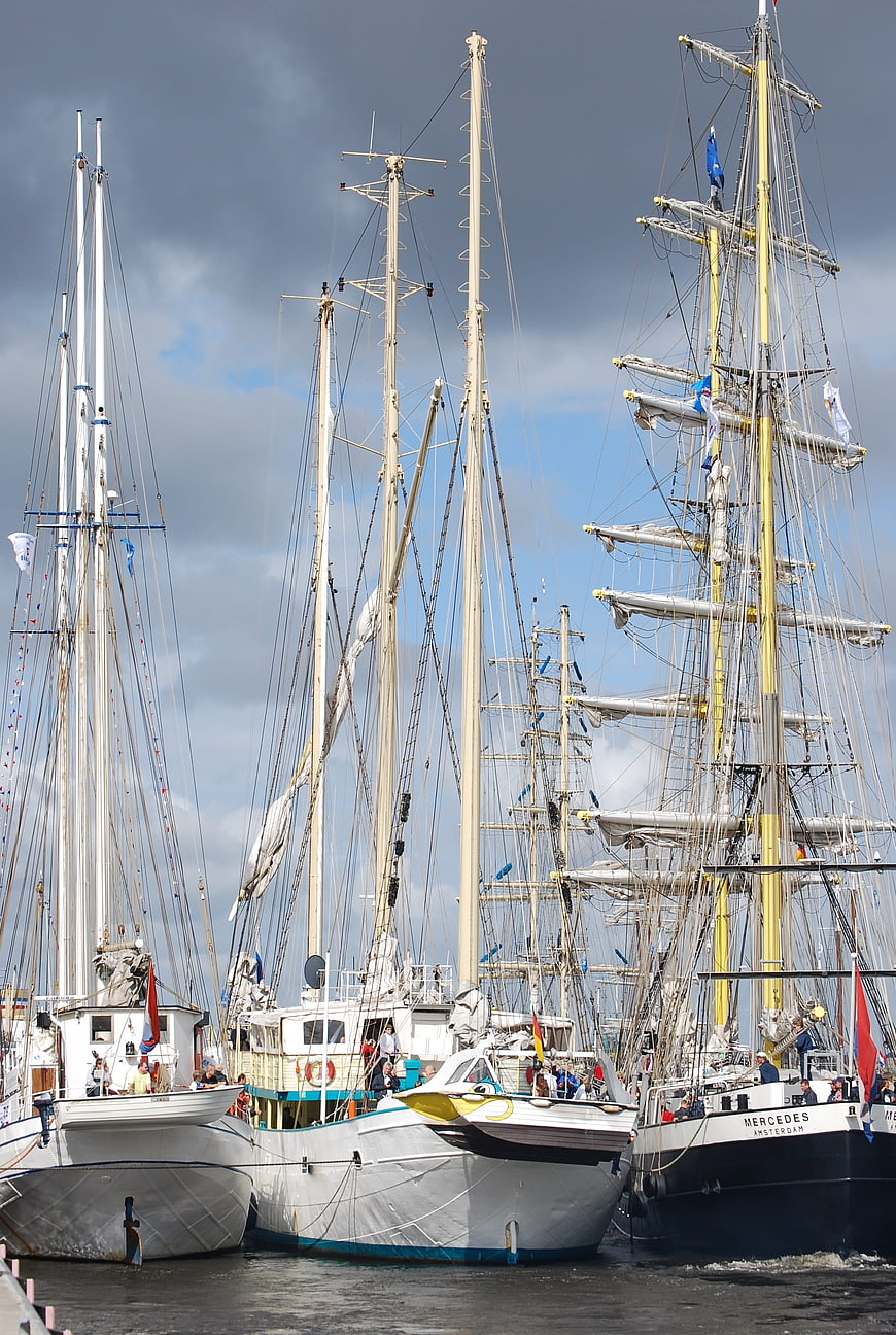 Tall sailing ships docked in harbor under cloudy sky