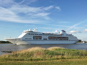 White cruise ship sailing on river with grassy foreground