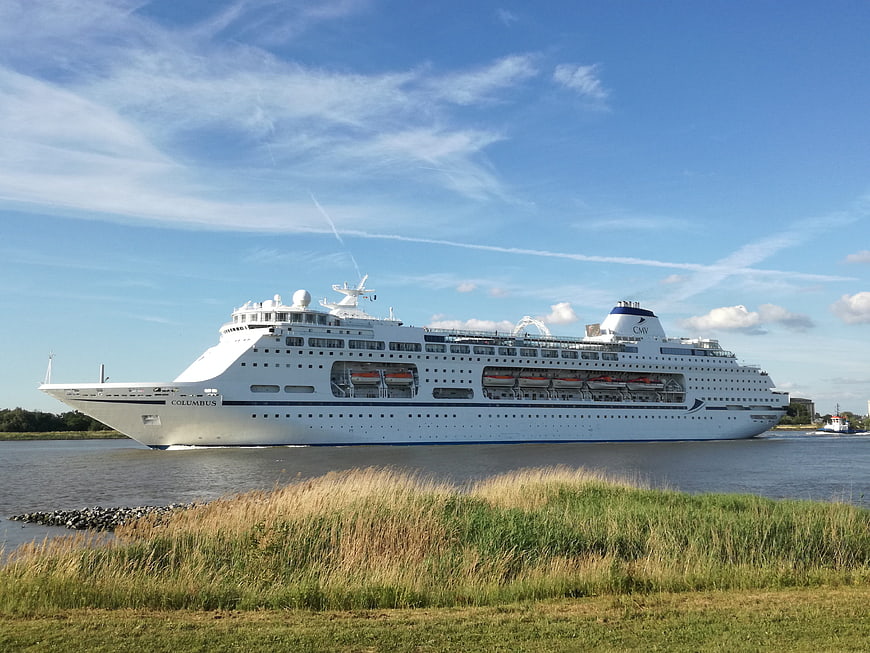 White cruise ship sailing on river with grassy foreground
