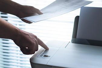 Hands pressing button on office printer with document