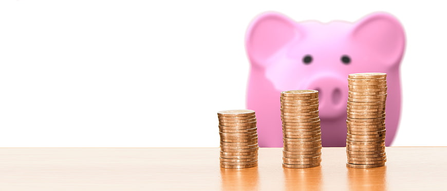 Stacks of coins and pink piggy bank on wooden table
