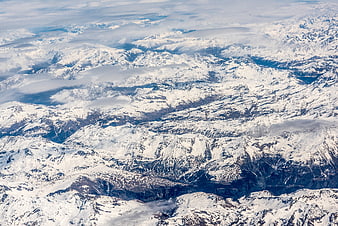 Aerial view of vast snow-covered mountain range with clouds