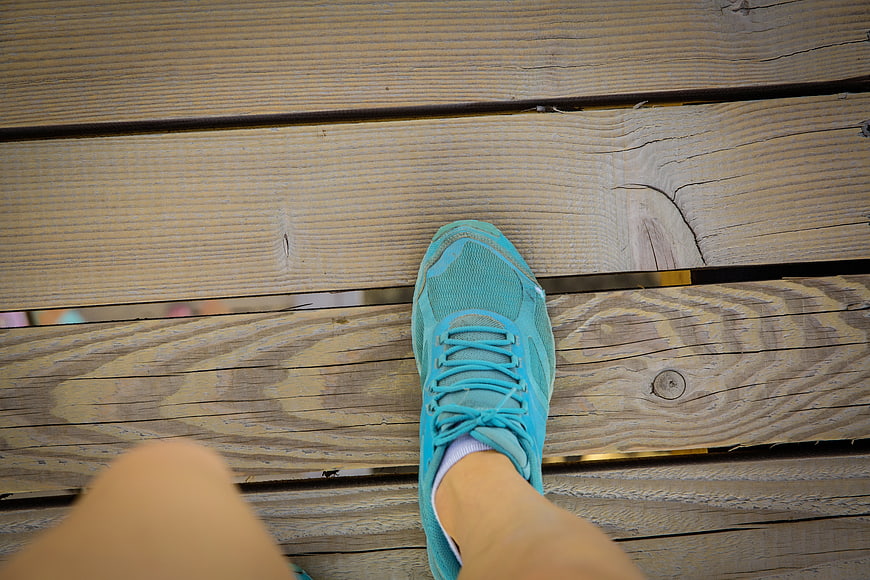 Blue running shoe on wooden deck from first-person perspective