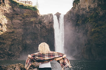 Woman with plaid blanket facing majestic waterfall in nature
