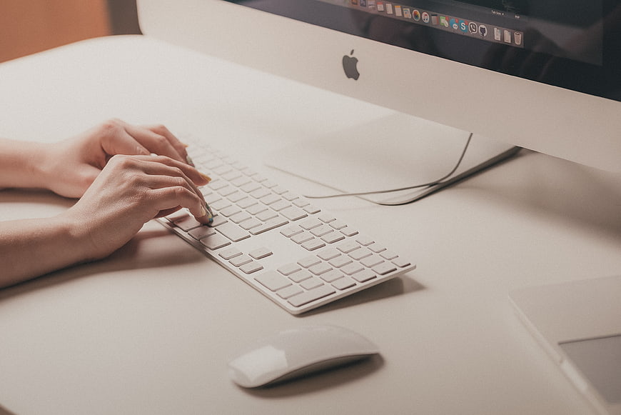 Hands typing on white keyboard at modern office desk