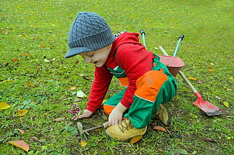 Young boy gardening with toy tools and flowers in autumn grass