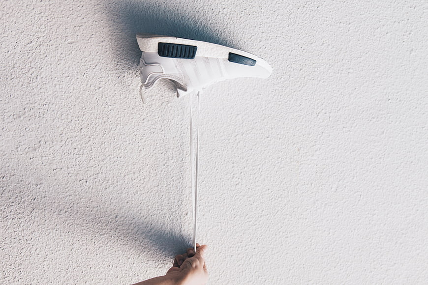 Hand Pulling White Sneaker Laces Against Textured Wall