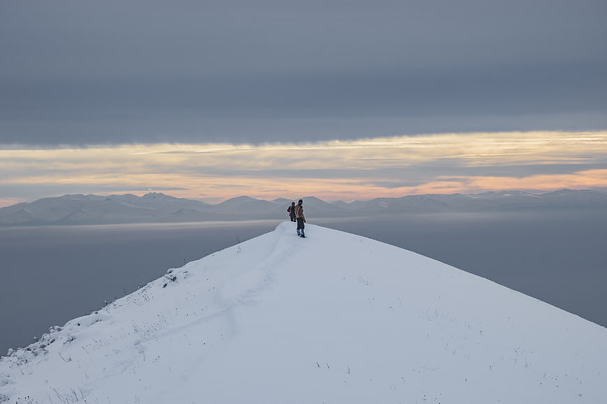 Hikers on Snowy Mountain Ridge at Sunset