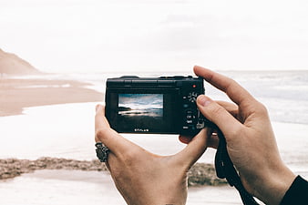Hands holding digital camera photographing beach landscape