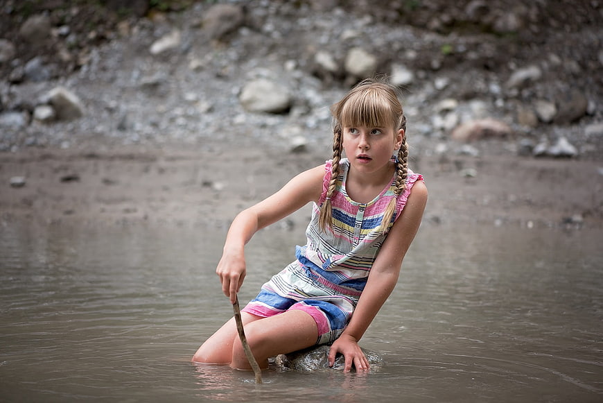 Young Girl with Braids Sitting in Shallow Stream