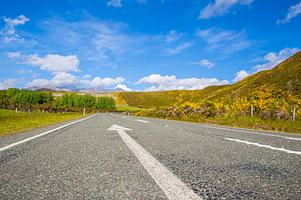 Empty asphalt road with arrow leading to mountains and yellow gorse