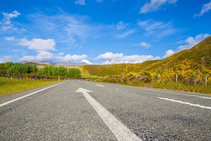 Empty asphalt road with arrow leading to mountains and yellow gorse