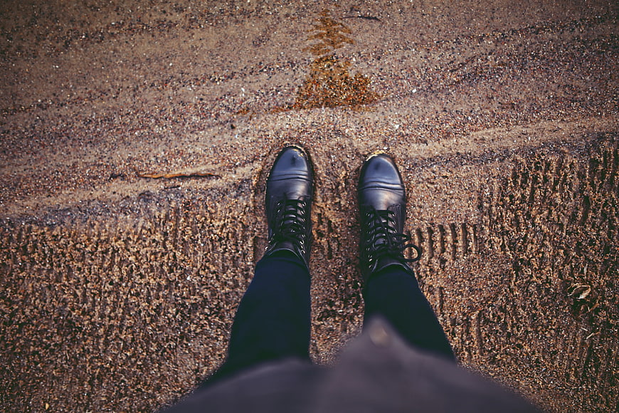 First-person view of black boots on sandy beach