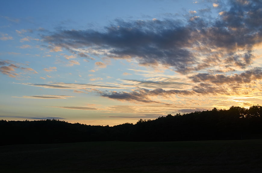 Dramatic sunset sky with clouds over dark forest silhouette