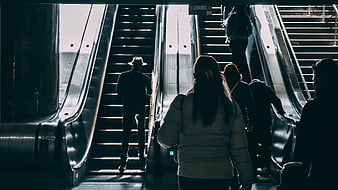 Silhouettes of people riding escalators in a subway station