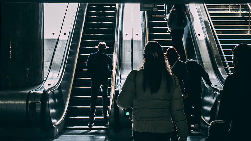 Silhouettes of people riding escalators in a subway station