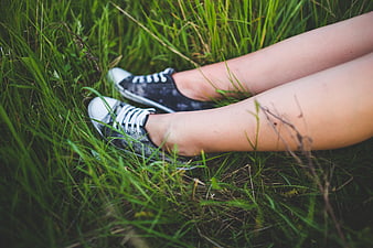 Girl legs in black sneakers sitting in green grass
