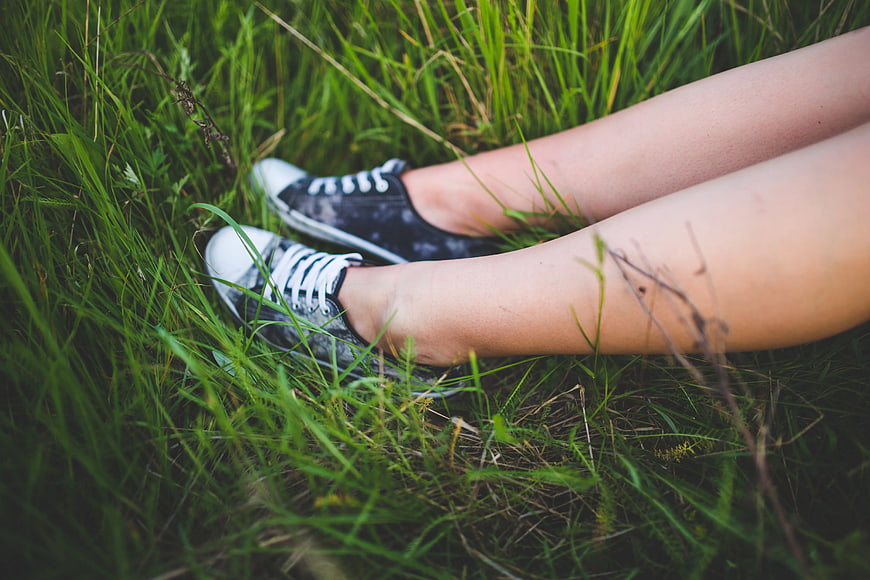 Girl legs in black sneakers sitting in green grass