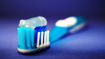 Close-up of blue toothbrush with gel toothpaste on blue background