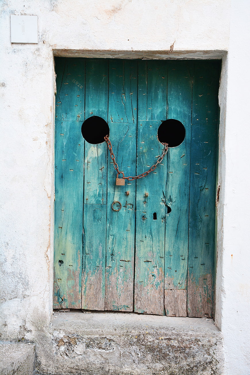 Old weathered teal wooden door with padlock and chain