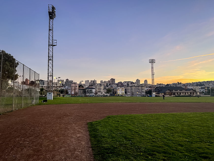 Urban baseball field at sunset with city skyline background