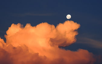 Full moon rising above vibrant orange sunset clouds