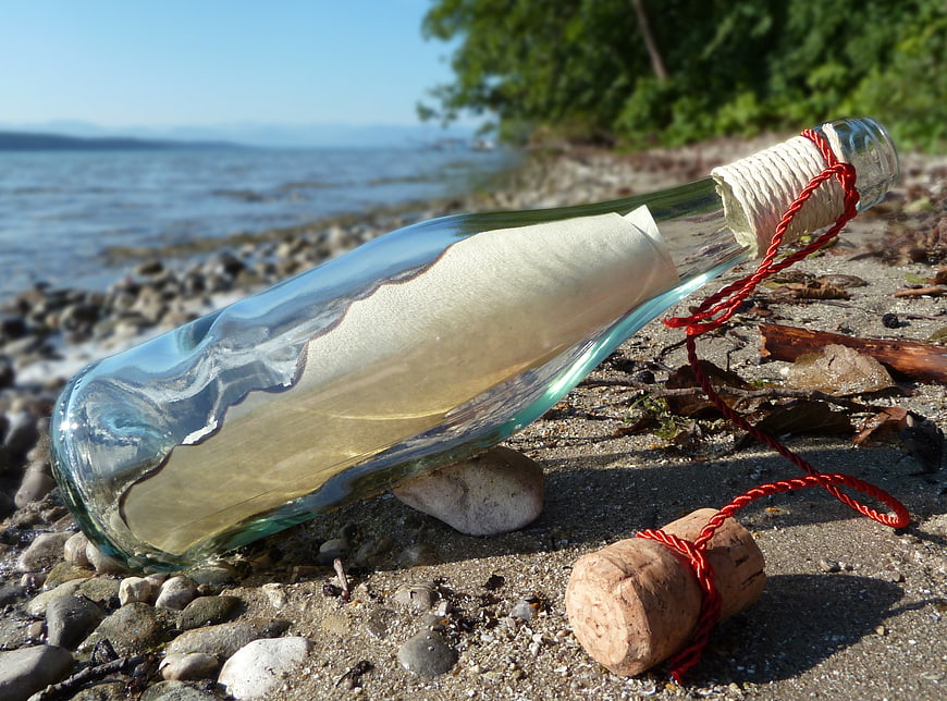 Message in a bottle on sandy beach with ocean background