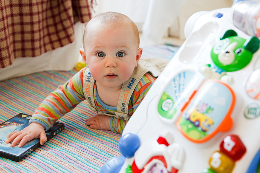 Cute baby playing with colorful toys on striped mat