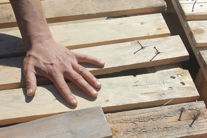 Carpenter's Hand Resting On Weathered Wooden Planks With Nails