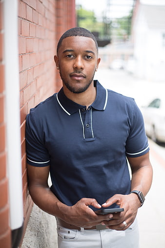 Confident Young Black Man Using Smartphone Against Brick Wall