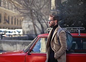 Handsome man with backpack leaning on red vintage car