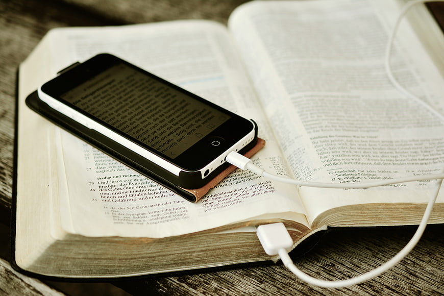 Smartphone with e-book app resting on open physical Bible