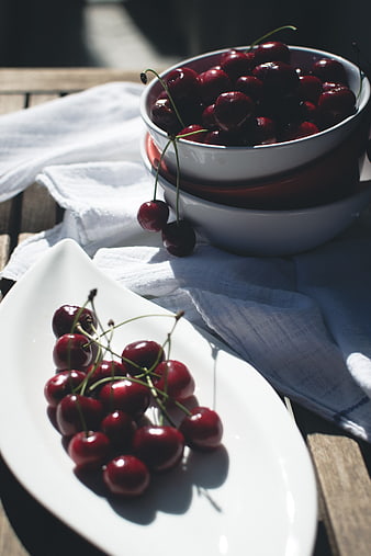Fresh red cherries in white bowls on wooden table
