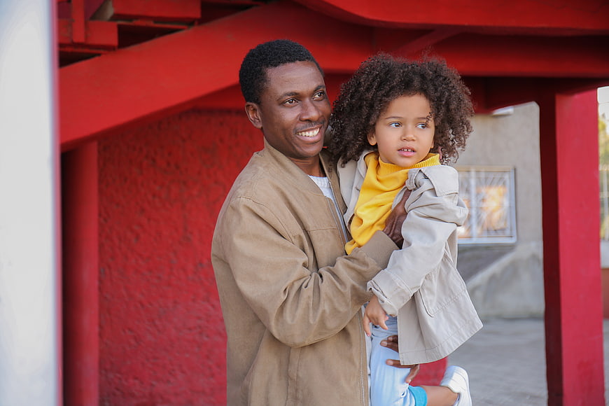 Happy Black Father Holding Young Daughter in Front of Red Wall