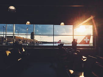 Silhouetted travelers in airport terminal watching Swiss planes at sunset
