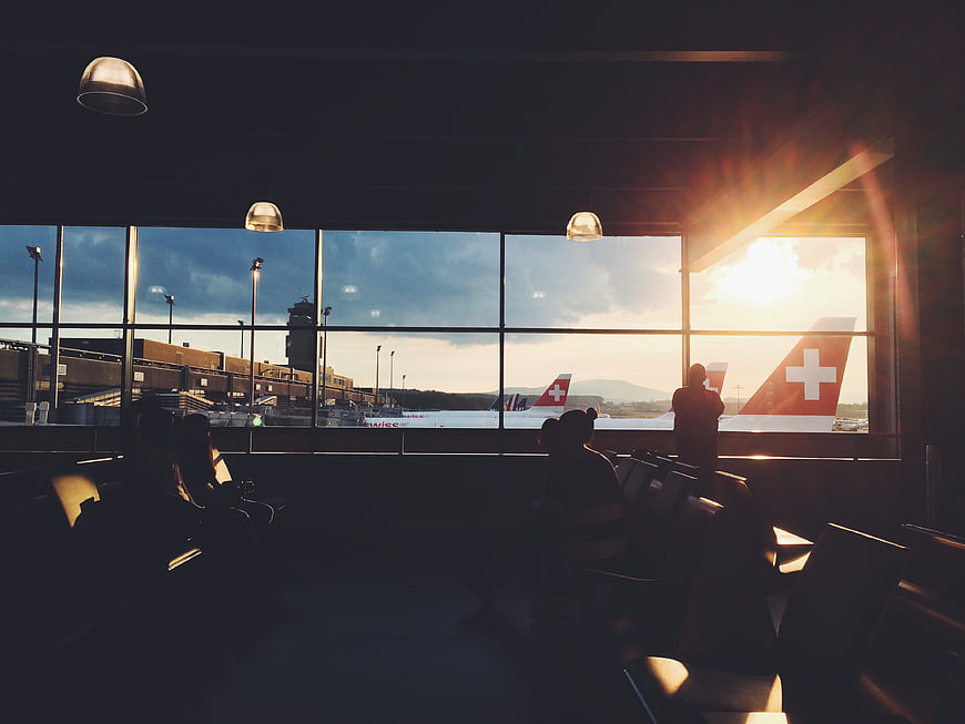 Silhouetted travelers in airport terminal watching Swiss planes at sunset