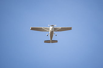 White propeller airplane flying against clear blue sky