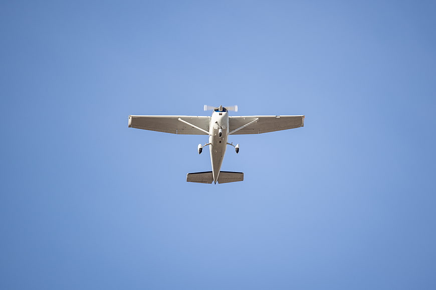 White propeller airplane flying against clear blue sky