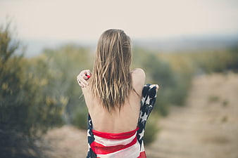 Woman wrapped in American flag looking at desert landscape