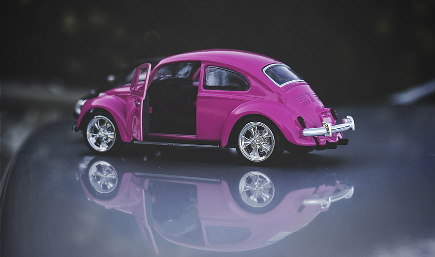 Pink toy Volkswagen Beetle with open door on reflective surface