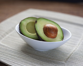Fresh Halved Avocado in White Bowl on Textured Mat