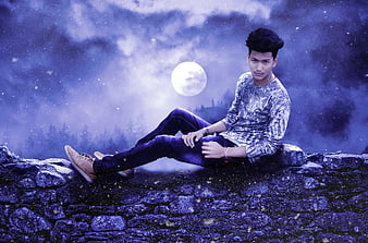 Young man sitting on stone wall under full moon night sky