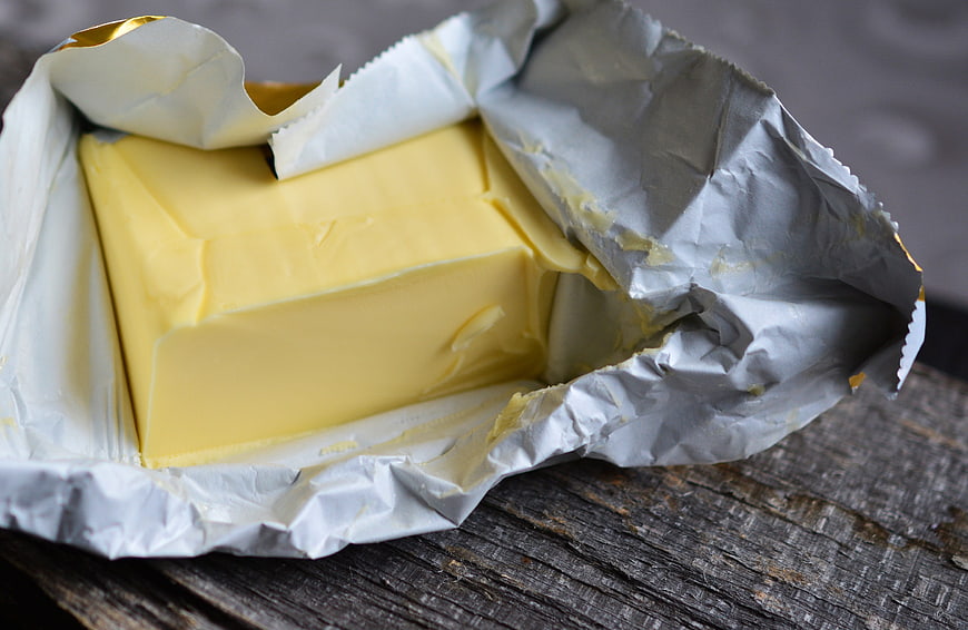 Block of butter in foil wrapper on rustic wood