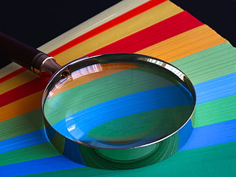 Magnifying glass on stack of colorful striped paper sheets