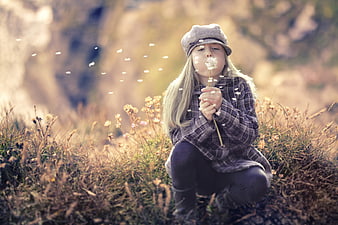 Cute girl blowing dandelion seeds in autumn meadow