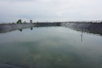 Wide shot of a large concrete reservoir with calm water and overcast sky