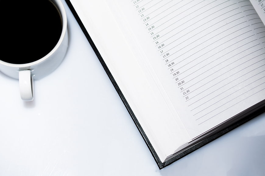 White coffee cup and open planner on white desk