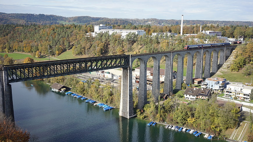 Train crossing stone viaduct over river in autumn landscape